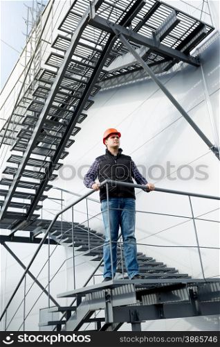 Male construction worker standing on steel staircase at factory