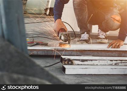 Male construction worker using electrical angle grinder for cutting iron bars with sharp fire sparks in construction site. Copy space wallpaper.