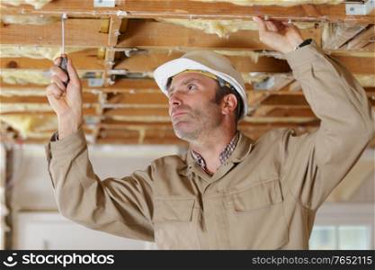 male construction worker using screwdriver on ceiling joist