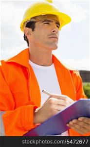 Male construction worker with clipboard looking away outside
