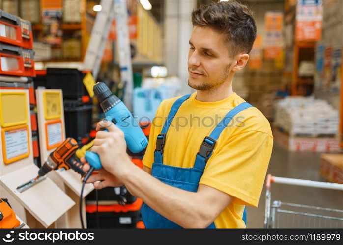 Male constructor choosing electric screwdriver in hardware store. Builder in uniform look at the goods in diy shop. Constructor choosing electric screwdriver, diy