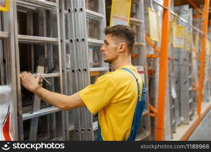 Male constructor choosing the stairs in hardware store. Builder in uniform look at the goods in diy shop. Constructor choosing the stairs in hardware store