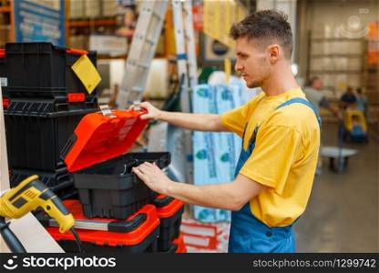 Male constructor choosing toolbox in hardware store. Builder in uniform look at the goods in diy shop