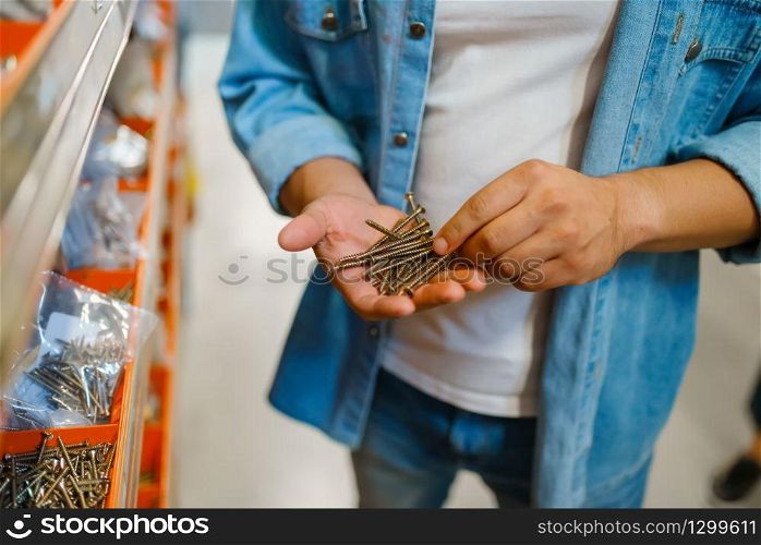 Male consumer buying tapping screws in hardware store. Customer look at the goods in diy shop, shopping in building supermarket