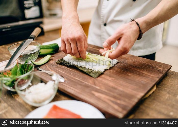Male cook hands, making sushi rolls, seafood. Traditional japanese cuisine, preparation process. Male cook hands making sushi rolls, seafood