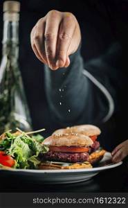 Male cook in a restaurant, decorating vegan burger with falling sesame. . Chef in Restaurant, Decorating Vegan Burger with Sesame
