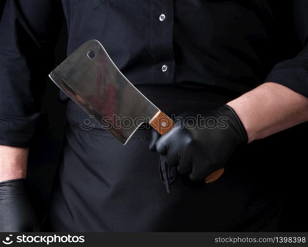 male cook in black uniform and black latex gloves holds a large sharp meat knife, close up