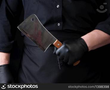 male cook in black uniform and black latex gloves holds a large sharp meat knife, close up