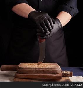 male cook in black uniform and black latex gloves holds a vintage sharp knife over a cutting board, black background