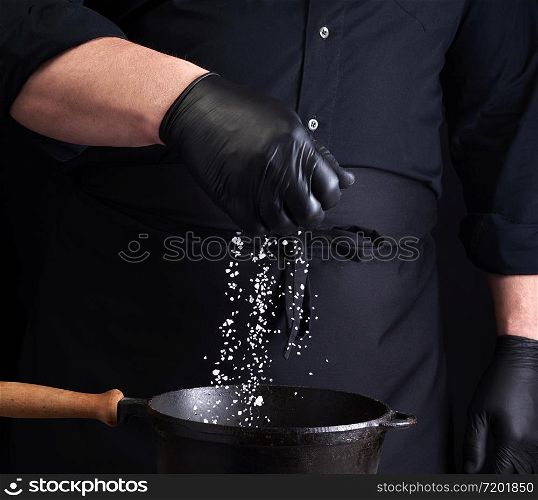 male cook in black uniform and latex gloves salt food in a black cast-iron pan, salt crystals froze in the air, low key