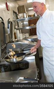 Male cook making chicken in frying pan in kitchen