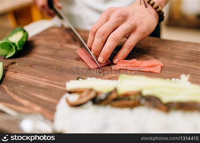 Male cook making sushi on wooden table, asian food. Traditional japanese cuisine, preparation process