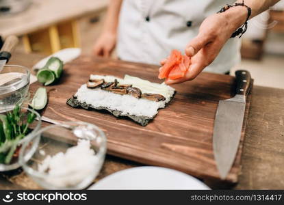 Male cook making sushi on wooden table, asian food. Traditional japanese cuisine, preparation process. Male cook making sushi on wooden table, asian food