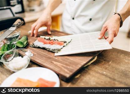 Male cook making sushi on wooden table, asian kitchen preparation process. Traditional japanese cuisine, seafood
