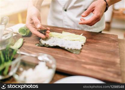 Male cook making sushi on wooden table, seafood preparation. Traditional japanese cuisine. Male cook making sushi on wooden table, seafood