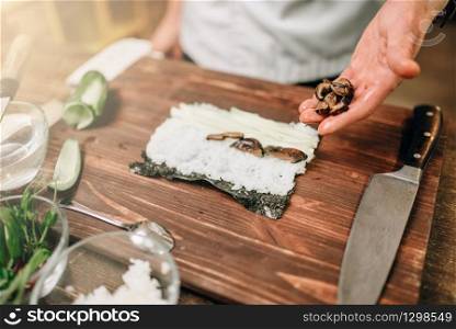 Male cook making sushi on wooden table, seafood preparation. Traditional japanese cuisine