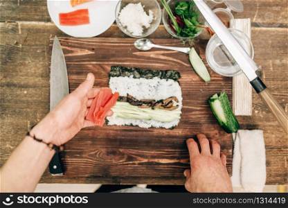 Male cook making sushi on wooden table, top view, asian food preparation process. Traditional japanese cuisine, seafood