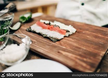 Male cook making sushi on wooden table, top view, asian food preparation process. Traditional japanese cuisine, seafood. Male cook making sushi on wooden table, top view