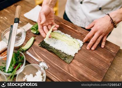 Male cook making sushi rolls on wooden table, seafood. Traditional japanese cuisine, preparation process