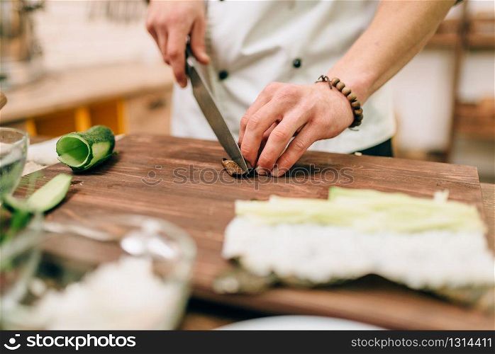 Male cook making sushi rolls on wooden table, seafood. Traditional japanese cuisine, preparation process. Male cook making sushi rolls on wooden table