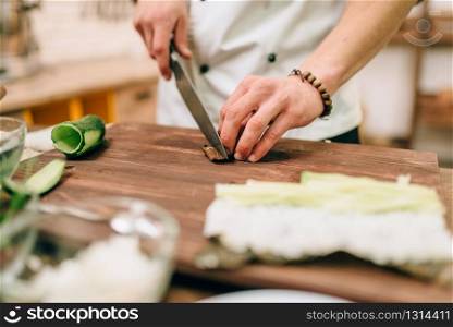 Male cook making sushi rolls on wooden table, seafood. Traditional japanese cuisine, preparation process. Male cook making sushi rolls on wooden table