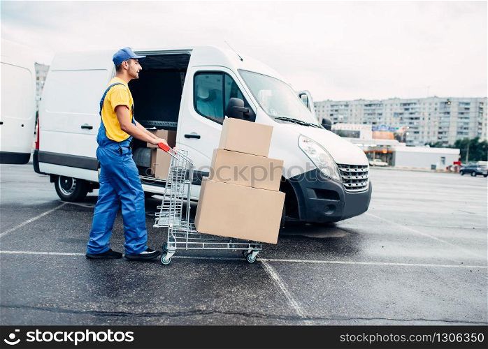 Male courier with parcel trolley against truck with carton boxes. Distribution business. Cargo delivery. Empty, clear containers. Logistic and post service