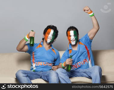 Male cricket fans with painted face in Indian tricolor enjoying game while having drink at home