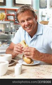 Male Customer Enjoying Sandwich And Coffee In Cafe