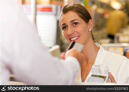 Male customer in supermarket handing his credit card to cashier at the checkout desk in order to pay