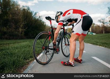 Male cyclist in helmet and sportswear adjusts the bike before competition. Workout on bike path, bycycle race