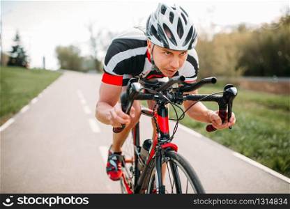 Male cyclist in helmet and sportswear rides on bicycle, front view. Workout on bike path, cycling. Male cyclist rides on bicycle, front view