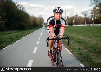 Male cyclist in helmet and sportswear rides on bicycle, front view. Workout on bike path, cycling