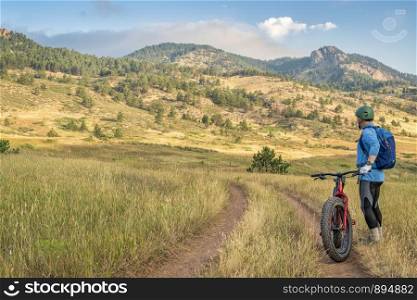 male cyclist with a fat mountain bike enjoying morning view of Rocky Mountains foothills at Lory State Park