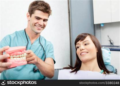 Male dentist explaining a female patient denture work in dental clinic. Dentist explains a female patient denture work in clinic