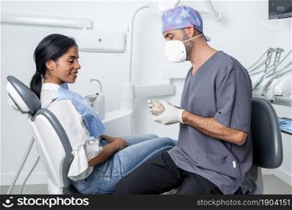 Male dentist showing a dental mould to a female patient sitting in a chair in a dental clinic. Dentist showing a dental mould to a patient sitting in a dental clinic.