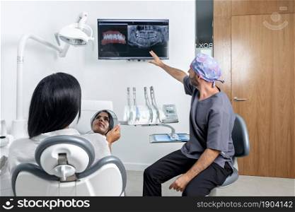 Male dentist showing a x-ray to a female patinet that is sitting on a chair in a clinic room. Dentist showing a x-ray to a patinet that is sitting on a chair in a clinic