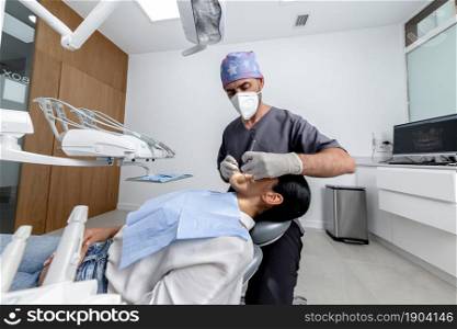Male dentist with uniform standing while examining the mouth of a female patient in a dental clinic. Dentist standing while examining the mouth of a patient in a dental clinic