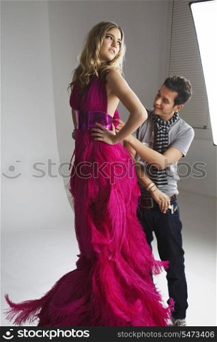 Male designer adjusting dress on fashion model in studio