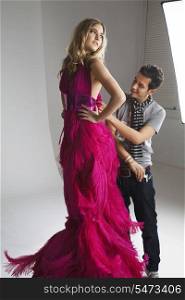 Male designer adjusting dress on fashion model in studio