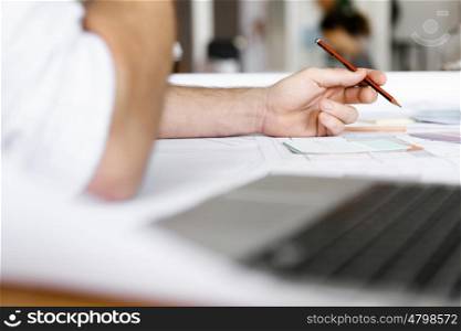 male designer working at desk. Male architect with computer studying plans in office