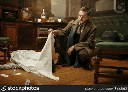 Male detective in coat looking on victim&rsquo;s body at the crime scene, retro style. Criminal investigation, inspector is working on a murder, vintage room interior on background. Detective looking on victim&rsquo;s body, crime scene