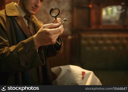 Male detective looks on evidence through magnifying glass at the crime scene, retro style. Criminal investigation, inspector is working on a murder, vintage room interior on background. Detective looks evidence through magnifying glass