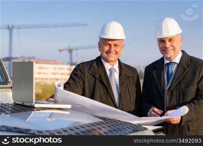 Male developers with blueprints at construction site discuss architect project