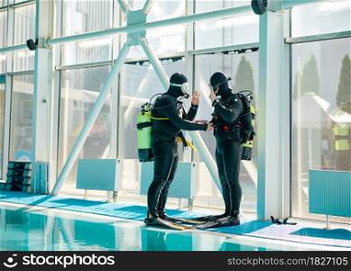 Male diver and divemaster in scuba gear, dive lesson in diving school. Teaching people to swim underwater, indoor swimming pool interior on background. Male diver and divemaster in scuba gear, diving