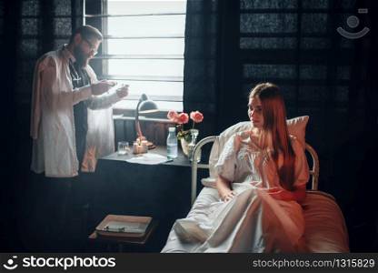 Male doctor against sick female patient in hospital bed. Illness of woman, clinic room, health recovery and treatment. Male doctor with syringe against sick woman in bed