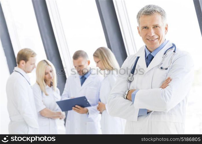 Male doctor and her team. Successful mature male doctor and his team on background in clinical office