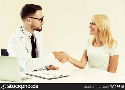 Male doctor doing handshake with female patient in hospital office. Healthcare and medical service.