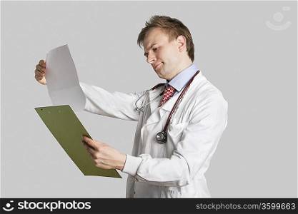 Male doctor in a lab coat reading medical records over gray background