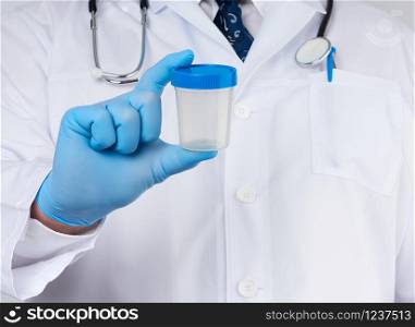 male doctor in a white coat and tie stands and holds a plastic container for urine specimen, wearing blue sterile medical gloves