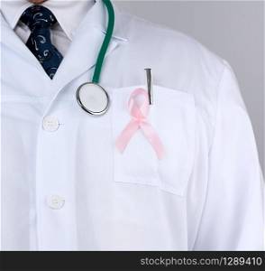 male doctor in a white coat and tie stands and holds a pink silk ribbon in the form of a loop, symbol of the fight against breast cancer in October